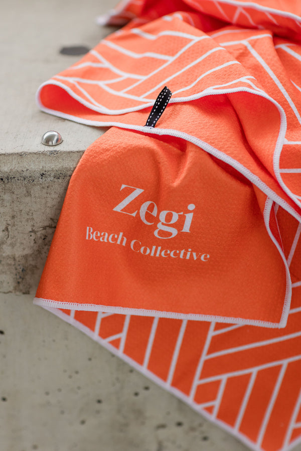 Orange gym towel draped over a step. Any time microbial super absorbent. With a corner zipper pocket